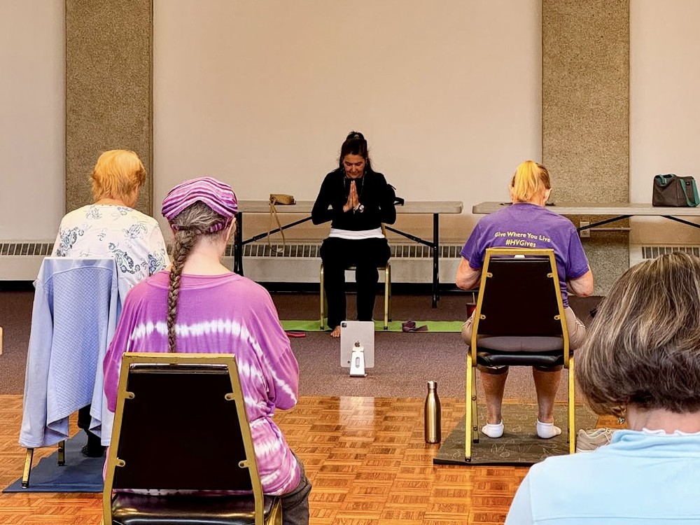 Miss Susan leading seated chair yoga with students in class.